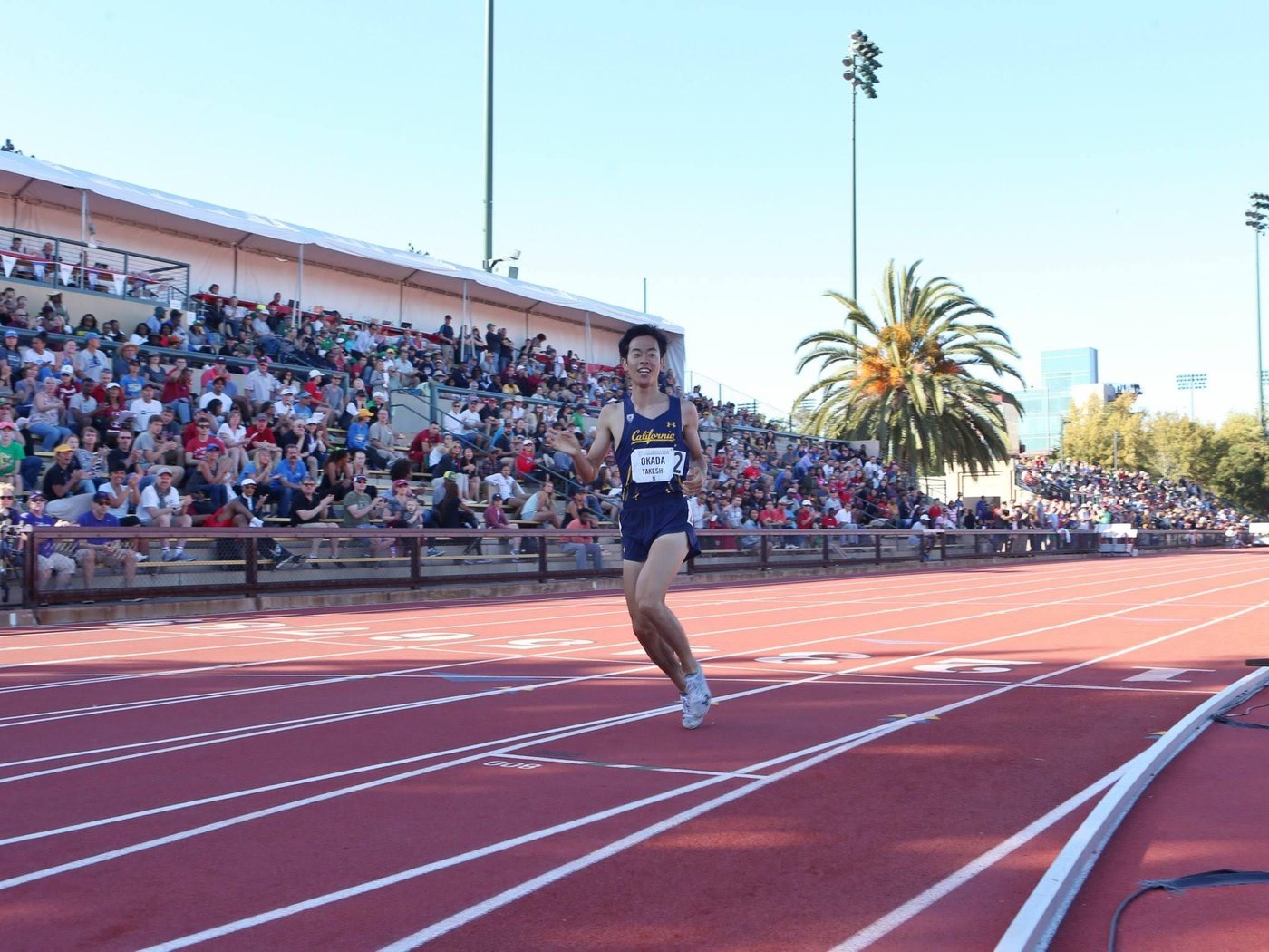 Takeshi Okada racing in a California singlet in front of a full stand